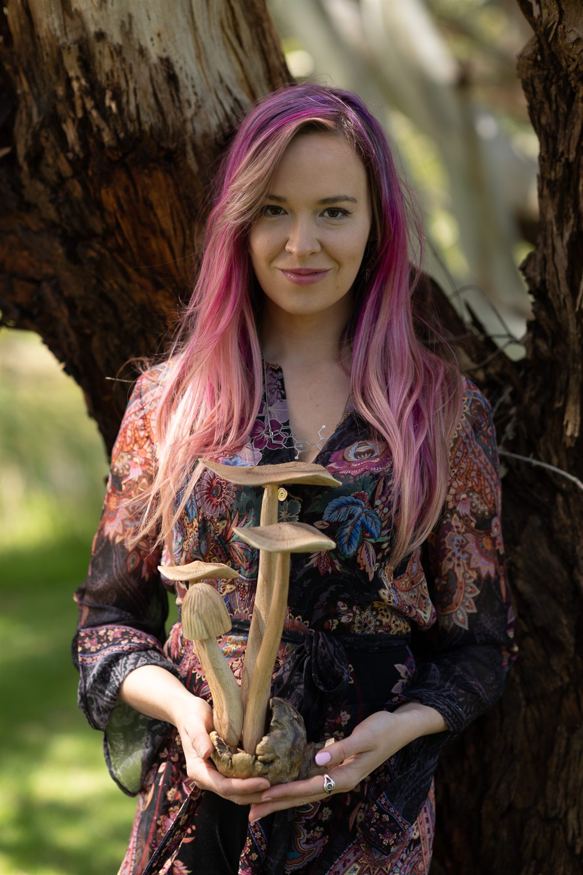 Melissa Warner in a garden, holding a carved wooden sculpture of mushrooms
